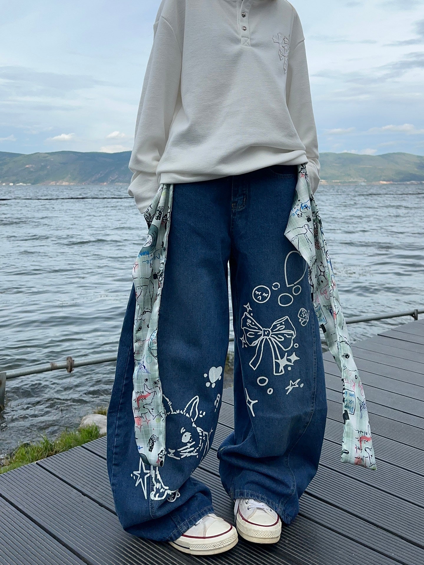 Graffiti strap-detailed curved wide-leg jeans.