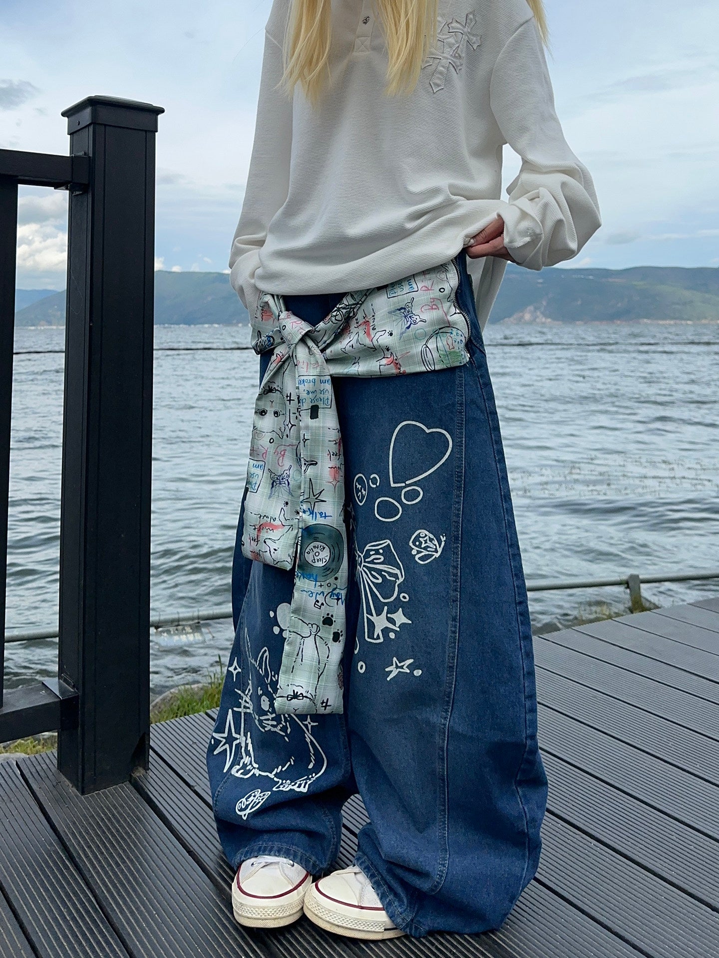 Graffiti strap-detailed curved wide-leg jeans.
