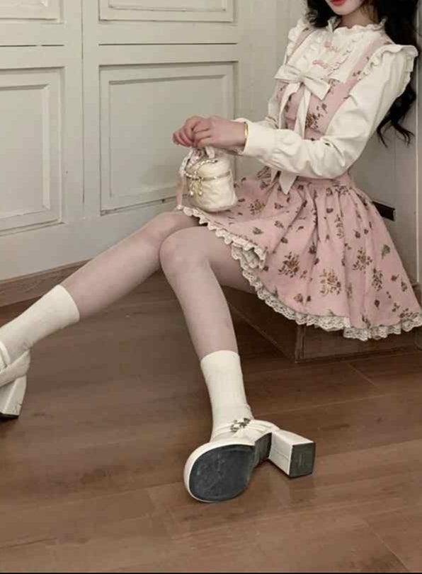 Woman in a pink floral dress sitting in a room with wooden floors and white paneled walls.
