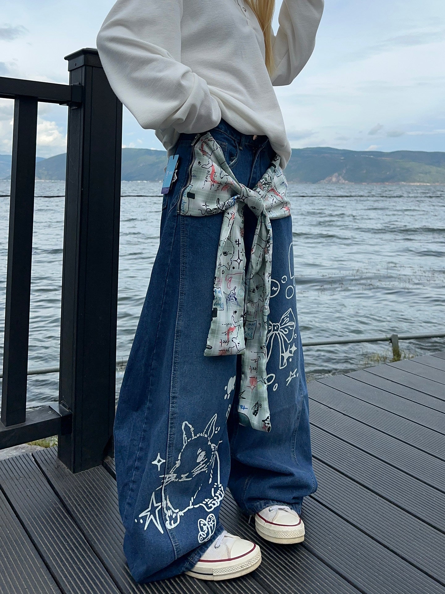 Graffiti strap-detailed curved wide-leg jeans.