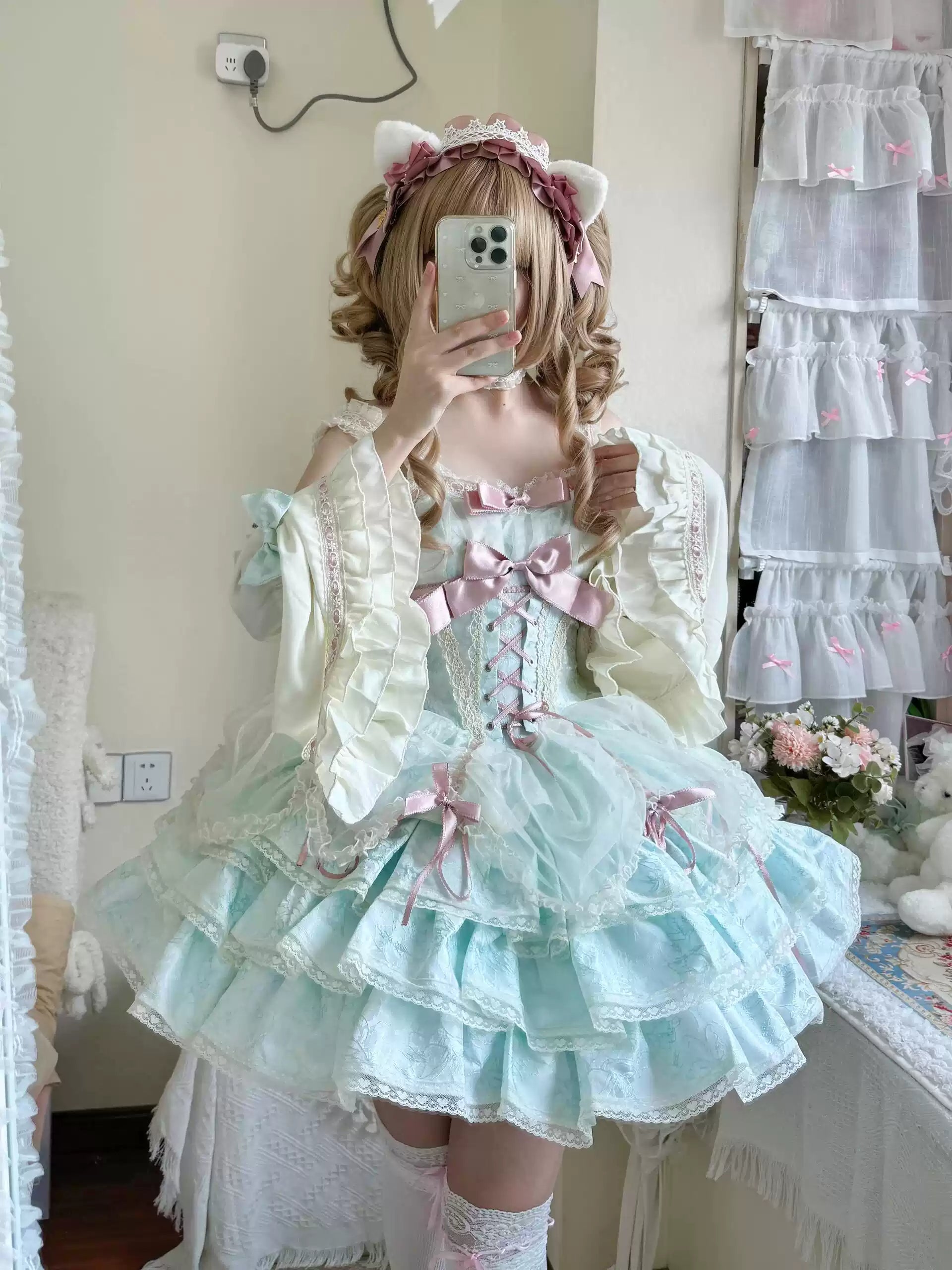 Person wearing a pastel-colored Lolita outfit with ruffles and bows, taking a mirror selfie.