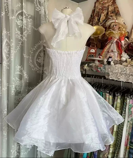 White dress on a mannequin with a large bow in a store setting.